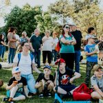 A diverse group of people enjoying a sunny day at an outdoor community event in a park setting.